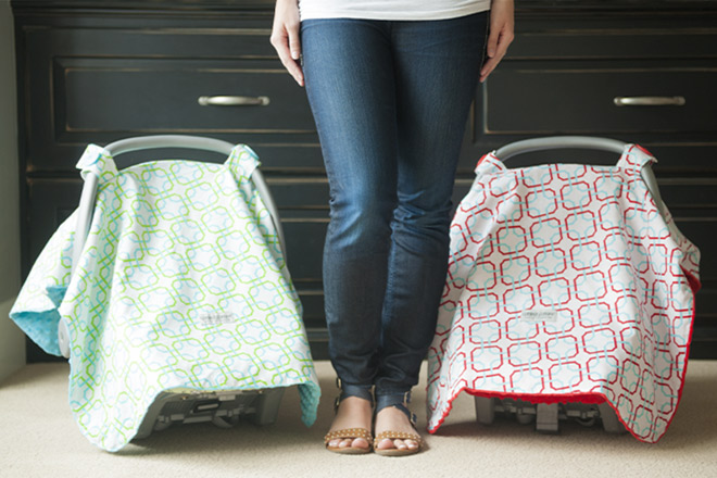 A Woman Standing Between Two Baby Carseats with Colorful Canopy Covers