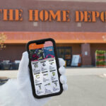 Hand Holding a Phone Showing Home Depot Black Friday 2023 Sales in Front of the Home Depot Store