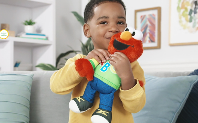 A Kid Smiling and Holding the Playskool Sesame Street Singing ABCs Elmo Plush