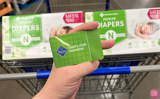 Hand Holding a Sam's Club Membership Card with Diapers in a Shopping Cart in the Background