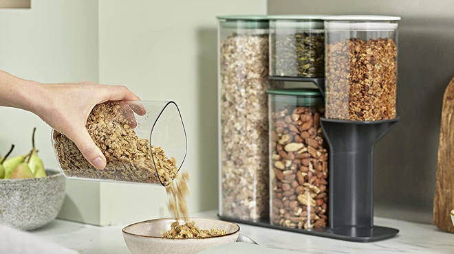 A Hand Pouring Food from Joseph Joseph Podium Storage Container plus Four Storage Containers with Food in Background