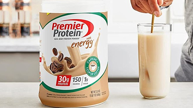 Premier Protein Powder Cafe Latte on a Table and a Man Making a Drink on the Left Side