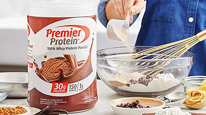 Premier Protein Powder in Chocolate Flavor on a Table with Woman Baking on the Left Side