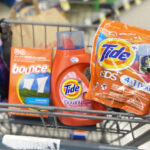 Hand Holding Tide Pods with Other Laundry Care Products in Cart