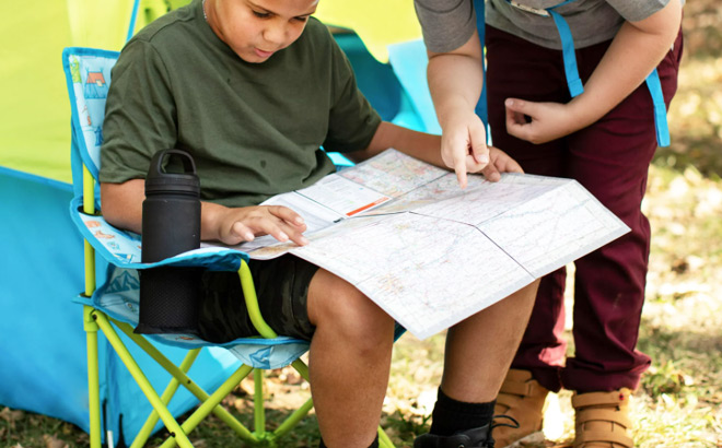 Boy Sitting on a Firefly Outdoor Gear Youth Camping Chair and Looking at a Map