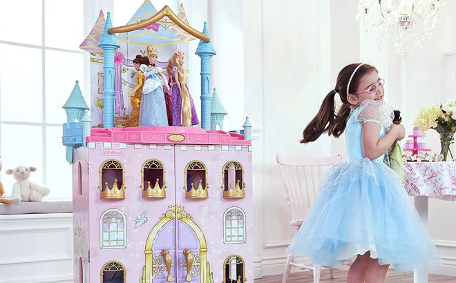 an Image of a Girl Beside a KidKraft Disney Princess Dance Dream Wooden Dollhouse