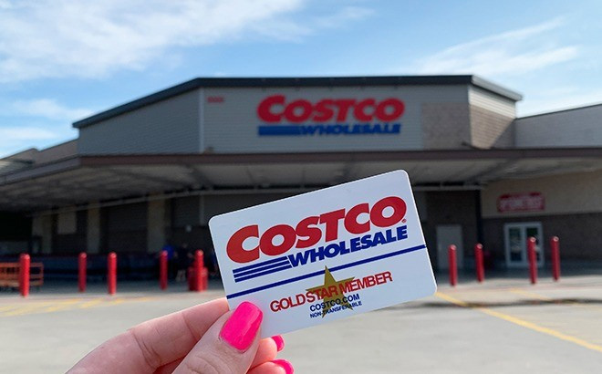 A Hand Holding a Costco Membership Card in Front of The Store