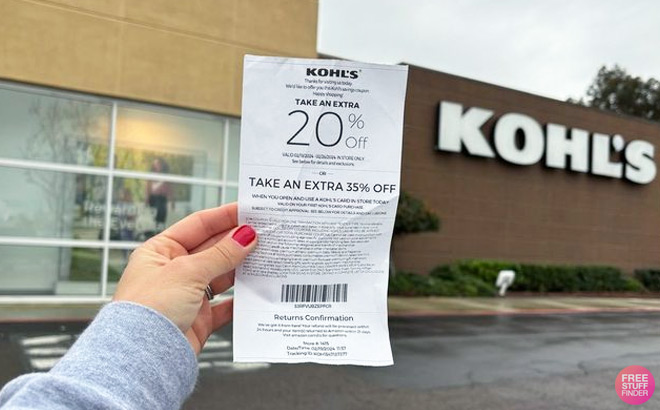 Hand Holding Kohls Coupons for 20 off In Front of Kohls Store Sign