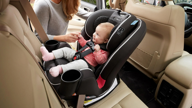 A mother holding a hand of a baby seated on aGraco TrioGrow SnugLock 3 in 1 Car Seat