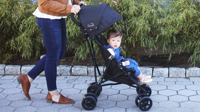 A mother pushing a Kolcraft 9 5 lb Umbrella Stroller with a toddler