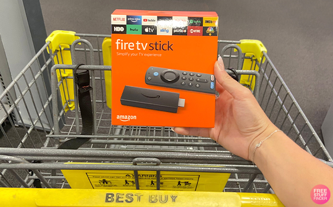 Hand Holding Amazon Fire TV Stick in front of Best Buy Cart