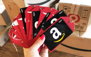 Hand Holding Amazon Gift Cards with Amazon Delivery Boxes in the Background