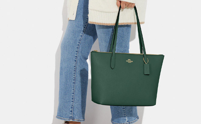 Woman is Holding Coach Zip Top Tote Bag in Dark Pine Color