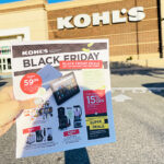 A Hand Holding the Kohls Black Friday Ad with a Kohls Store in the Background