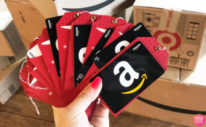 Hand Holding Multiple Amazon Gift Cards with Amazon Delivery Boxes in the Background