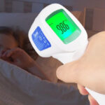 Lady Checking the Sleeping Girls Temperature Using a Berrcom Infrared Forehead Thermometer