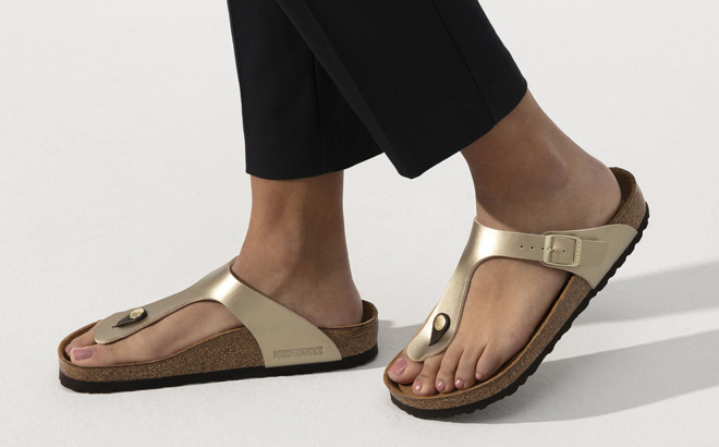 Woman is Wearing Birkenstock Gizeh Narrow Birko Flor Sandal in Gold Color