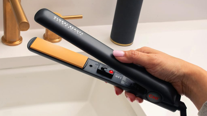 A Person Holding CHI Ceramic Hair Iron Over a Bathroom Sink