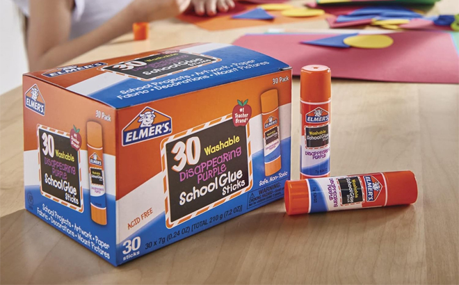 Elmers Disappearing Purple School Glue Sticks 30 Count on a Table with Kids in the Background
