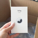 Hand Holding Apple Airtag 4 Pack in Front of Amazon Box