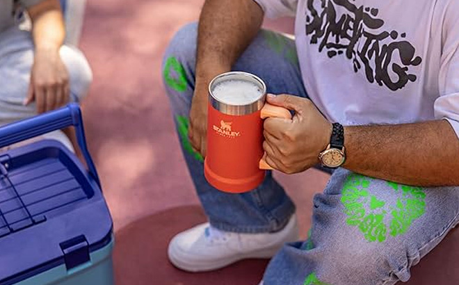 Hand Holding Stanley Adventure Big Grip Beer Stein 24 oz in Tigerlily Color