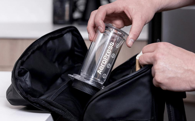 A Person Putting the AeroPress Tinted 3 in 1 Brewing Coffee Press in a Duffel Bag