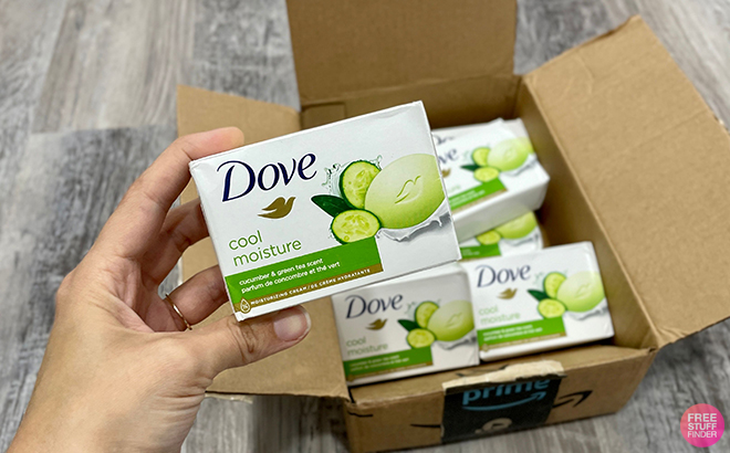 Hand Holding Dove Cool Moisture Bar Soap with Amazon Shipping Box in the Background Filled with More of the Same Soap