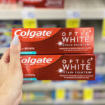 Hand Holding Two Colgate Optic White Stain Fighter Toothpaste