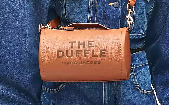 A Closeup of Marc Jacobs The Leather Duffle Bag Being Carried by a Person Wearing Denim Jeans and Jacket