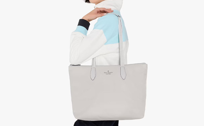 A Person is Holding Kate Spade Mel Packable Tote in Platinum Grey Color