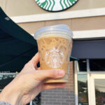 A Person Holing a Cup of Starbucks Coffee in Front of a Starbucks Store