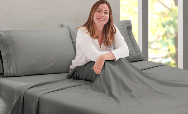 A Person Sitting on the Nestl Queen 4 Piece Bed Sheet Set in the Color Gray