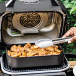 A Person getting Food out of Ninja 7 in 1 Master Outdoor Grill and Smoker