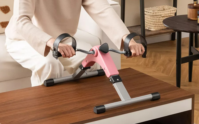 A Woman Using the Costway Under Desk Exercise Bike in Pink