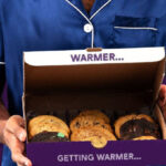 A person wearing PJs holding a box of Insomnia Cookies