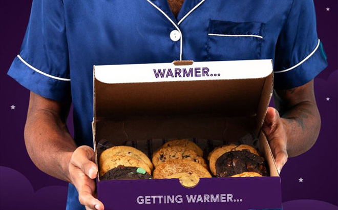 A person wearing PJs holding a box of Insomnia Cookies