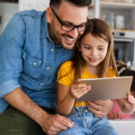 Father and Daughter Looking at a Tablet and Smiling
