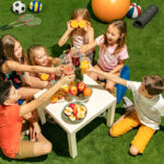 Kids Sitting at a Table with Drinks and Food on the Grass