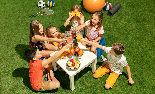 Kids Sitting at a Table with Drinks and Food on the Grass