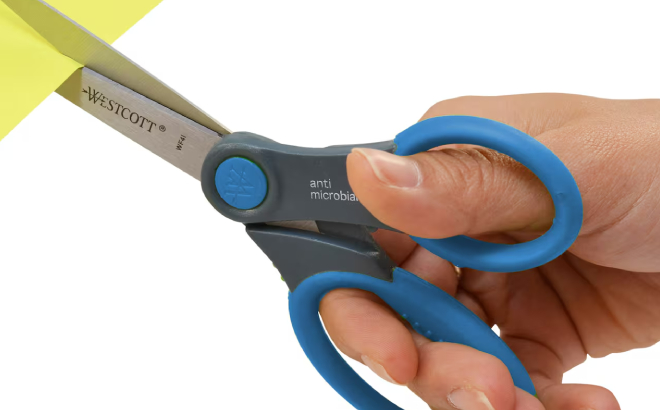 A Person Cutting a Colored Paper Using Westcott Scissors