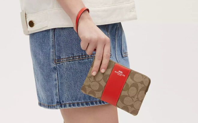 A Person Holding a Coach Outlet Corner Zip Wristlet In Signature Canvas