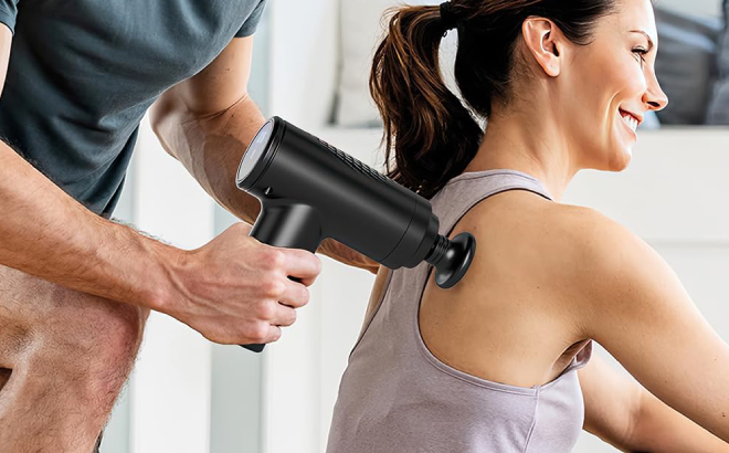 A Person Massaging a Womans Back Using a Mini Massage Gun