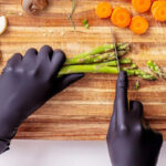 A Person cutting vegetables with Black Gloves on