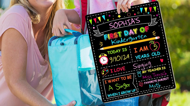 A kid holding a Melisher Double Sided First of School Chalkboard