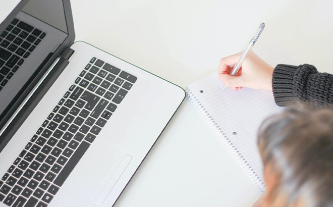 Person taking notes next to their Laptop