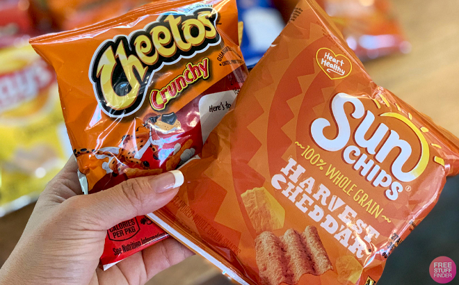 A Hand holding a Bag of Cheetos Crunchy Chips and a Bag of Sun Chips Harvest Cheddar