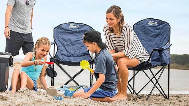 A Lady Sitting on a Coleman Portable Camping Chair while her family is playing on the beach