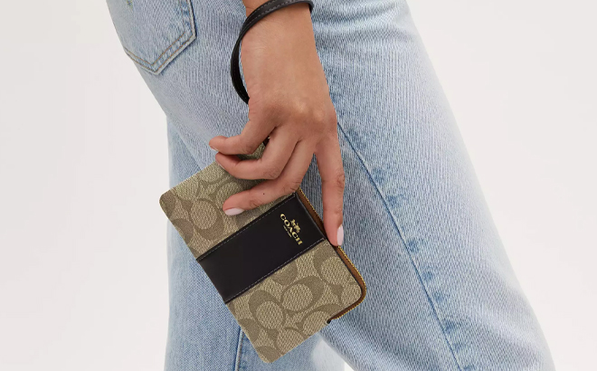 A Woman Holding Coach Outlet Corner Zip Wristlet In Signature Canvas