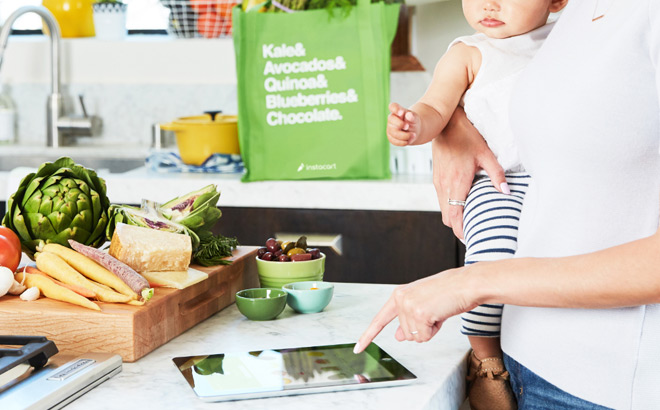 A Woman Holding a Child in the Kitchen and Looking at Her Tablet