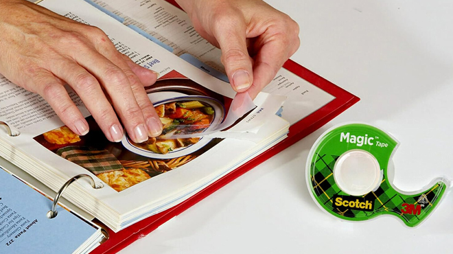 A person a fixing a page of a book using a Scotch Magic Tape